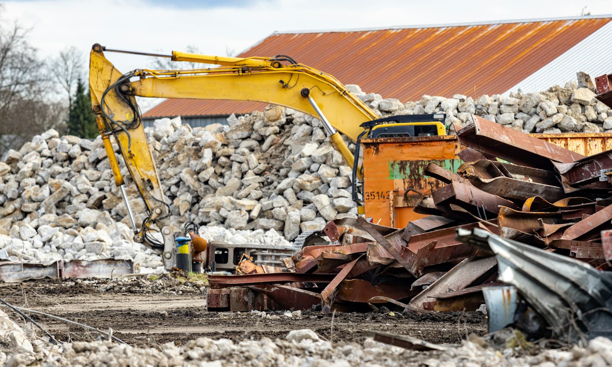 Demolition site with piles of concrete rubble and stacked scrap steel awaiting removal